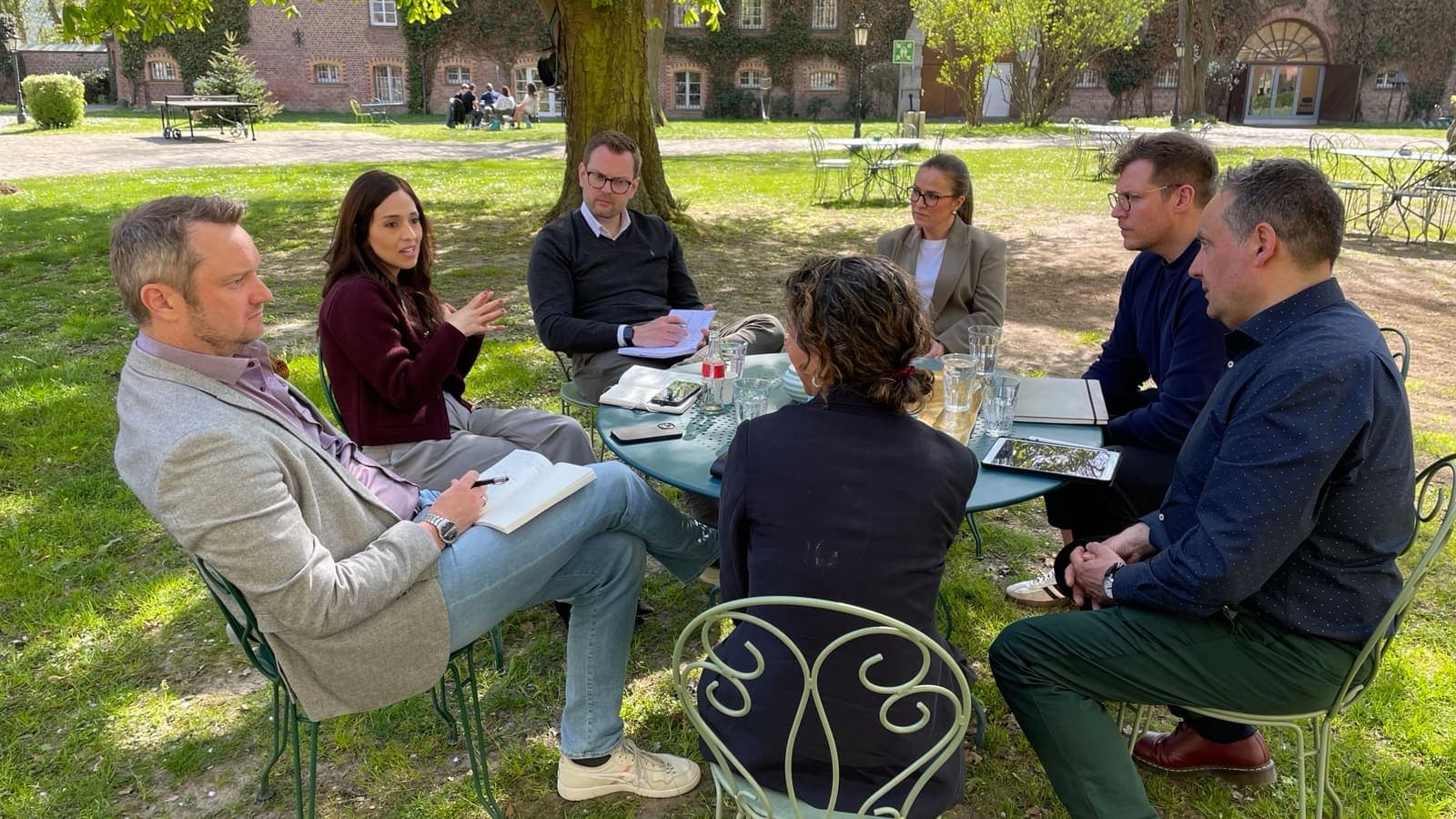 Natasha in conversation with a group of commercial leaders seated around a garden table, notebooks open