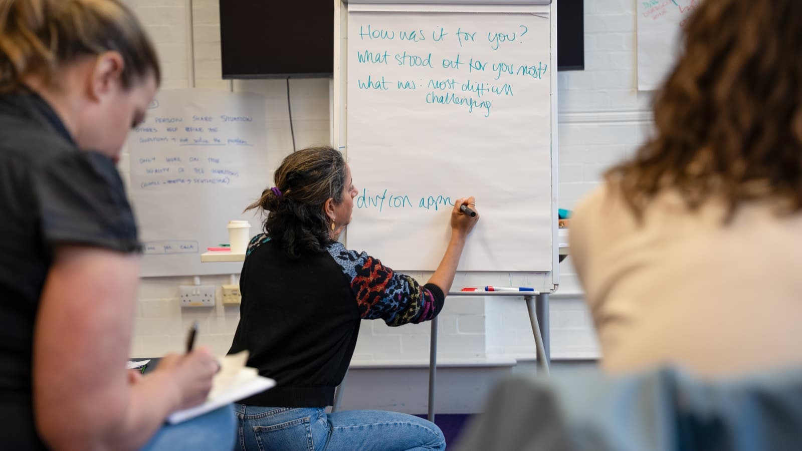 Natasha writing workshop questions on a flip chart while facilitating a small leadership group